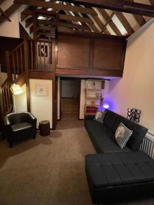 a living room with a black couch and a chair at Cosy Cottage next to Farmers Arms Country pub. in Gloucester