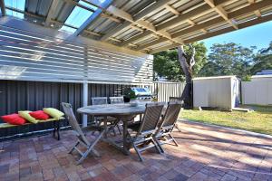 un patio con mesa de madera y sillas en Sandy Toes Beach House Jervis Bay - 2min to Beach, en Callala Beach