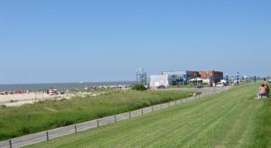 ein grasbewachsenes Feld mit Leuten, die am Strand spazieren in der Unterkunft Weinhaus Hotel in Norddeich