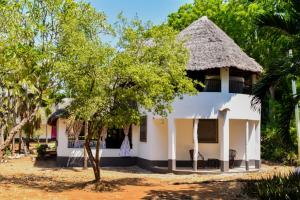 a white house with a thatched roof at Private room in a villa in Diani Beach