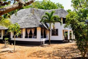 a white house with a thatched roof and palm trees at Double room in a villa in Diani Beach