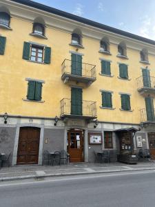 a yellow building with green windows and tables and chairs at El Rocol in Vezza dʼOglio