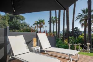 zwei weiße Stühle auf einer Terrasse mit Palmen in der Unterkunft Paradis en Rez de jardin - Standing - Vue Mer - piscine privée in Vallauris