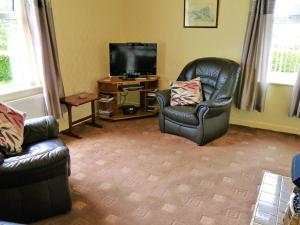 a living room with two chairs and a flat screen tv at Woodhall Cottage in Annan