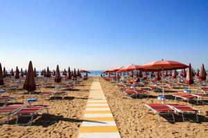 una spiaggia sabbiosa con sedie, ombrelloni e l'oceano di Jesolo Sun Beach House - Host Solution a Lido di Jesolo