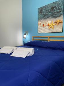 Una cama azul con toallas y una pintura en la pared. en SyracuseApartments IL PASUBIO di SIRACUSA Stupendo appartamento vicino ad ORTIGIA a 200m dal MARE, en Siracusa