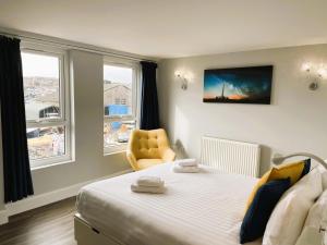 a bedroom with a bed and a chair and two windows at Kema Cottage in East Cowes