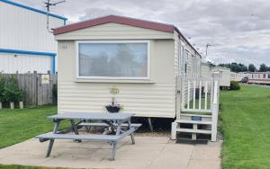 a tiny house with a picnic table and a bench at Oasis S108 Caravan, Golden Palm Resort in Chapel Saint Leonards