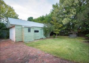 a small green building in a yard with a brick driveway at Cheerful 3 bedroom home in the centre of town in Shepparton