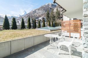 um pátio com uma mesa, cadeiras e montanhas em Haus Whymper em Zermatt