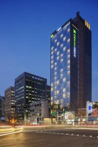 ソウルにあるibis Styles Ambassador Seoul Myeong-dongの横に緑の看板が立つ高層ビル