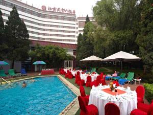 a swimming pool with red chairs and tables and a large building at CITIC Hotel Beijing Airport in Shunyi