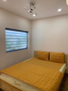 1 dormitorio con 1 cama con colcha amarilla y ventana en Nhà Nghỉ Ngọc Ánh, en Ấp Tam Tân