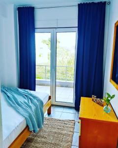 Villa Ulyana Toroni - Front seaview, First line, Fireplace في توروني: غرفة نوم بسرير ونافذة ذات ستائر زرقاء