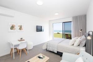 a white bedroom with a bed and a table and chairs at Views over Tasman, New luxury boutique studio overlooking the Tasman Sea in Greymouth