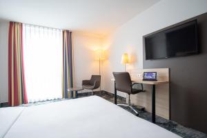 ein Hotelzimmer mit einem Bett, einem Schreibtisch und einem TV in der Unterkunft Taste Hotel Heidenheim in Heidenheim