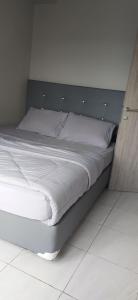 een bed met witte lakens en een houten hoofdeinde bij Newton Apartment Residence By Ayulian in Bandung