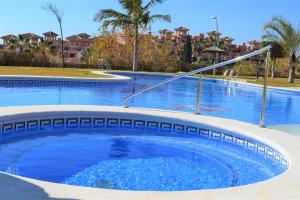 een zwembad met blauw water in een resort bij Espacioso apartamento con preciosos jardines y BBQ in Isla Plana
