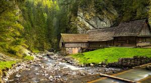 a wooden cabin next to a river in a mountain at Turistická ubytovňa in Liptovský Mikuláš