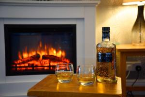 a bottle of whiskey and two glasses on a table with a fireplace at Fladda Chuain Holiday Home in Kilmuir