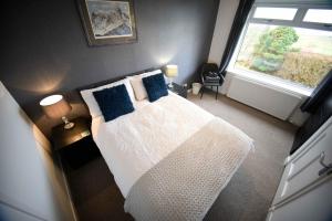 a bedroom with a white bed with blue pillows and a window at Fladda Chuain Holiday Home in Kilmuir