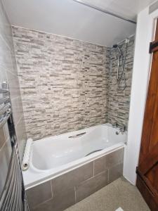 uma banheira branca na casa de banho com uma parede de tijolos em Ash Cottage em Hope