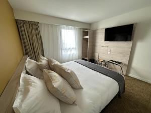 een slaapkamer met een wit bed met kussens en een televisie bij Hôtel Akena Chauray-Niort in Chauray