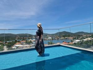 a woman standing on the edge of a swimming pool looking out at the city at Flat Samba Bossa Nova in Cabo Frio