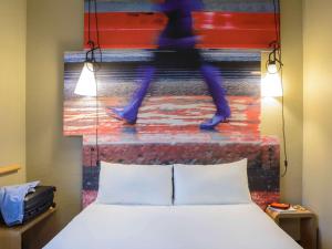 a bed in a room with a painting of a person walking down a stairs at Ibis Milano Centro in Milan