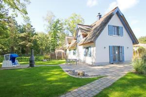 a white house with a grassy yard with a grill at Ferienhaus Stranddistel Haus - Terrasse, Garten, Sauna in Klein Gelm