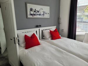 two white beds with red pillows in a bedroom at Edelweiss Guest House in Southend-on-Sea