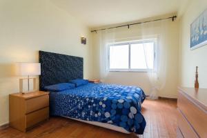 een slaapkamer met een bed met een blauw dekbed en een raam bij apartment with breathtaking view in Burgau