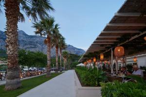 a street with palm trees and a restaurant with mountains in the background at Hotel Osejava in Makarska