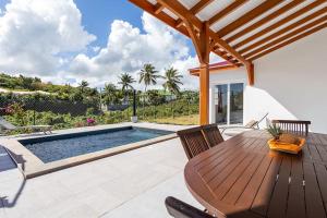eine Terrasse mit einem Holztisch und einem Pool in der Unterkunft villa de prestige Anse ka'nel in Le Moule