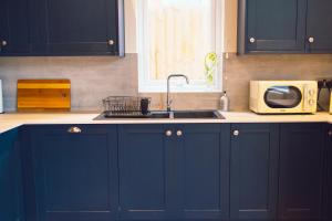 cocina con armarios azules, fregadero y microondas en The Milkmans Residence en Bournemouth