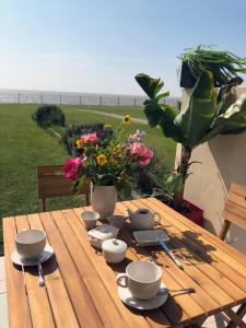 une table en bois avec des tasses, des soucoupes et des fleurs. dans l'établissement Studio-terrasse 3* bord de mer Châtelaillon plage, à Châtelaillon-Plage