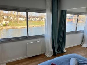 a bedroom with three windows with a view of a river at Sur le Loing in Moret-sur-Loing
