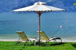zwei Stühle unter einem Regenschirm neben dem Wasser in der Unterkunft Hotel Du Lac - Relax Attitude Hotel in Brenzone sul Garda