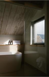 La salle de bains est pourvue d'une baignoire blanche et d'une fenêtre. dans l'établissement Brut the lodges, à Reijmerstok