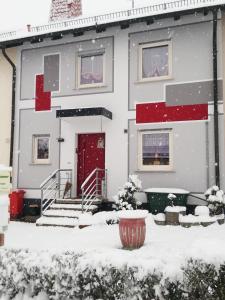 una casa con una puerta roja en la nieve en Monteurzimmer Beate Ackermann en Hochstadt am Main