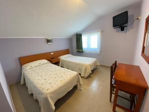 a room with two beds and a desk and a television at Hotel Chiquín in Tapia de Casariego