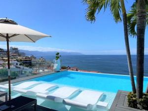 a pool with chairs and an umbrella and the ocean at New Zona Romantica beautiful Sunsets private Spa in Puerto Vallarta