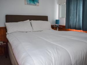 - un grand lit blanc avec des draps blancs et des rideaux bleus dans l'établissement Sandy Toes, à Scratby