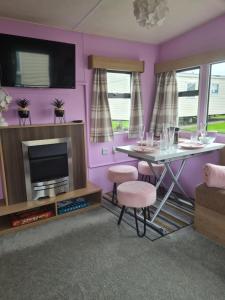 sala de estar con paredes de color rosa, mesa y TV en Lovely caravan at Harts Holiday Park Leysdown-on-Sea en Leysdown-on-Sea