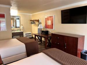 Habitación de hotel con 2 camas y escritorio con TV. en Abby's Anaheimer Inn - Across Disneyland Park, en Anaheim