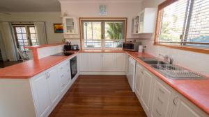 a kitchen with white cabinets and a wooden floor at Picnic Cottage, Lovely Home Near The Beach in Picnic Bay