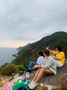 Trzy osoby siedzące na skale z widokiem na ocean w obiekcie GIA THÀNH HOMESTAY w Hoi An