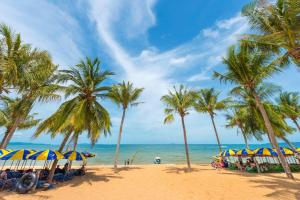 a beach with palm trees and chairs and the ocean at Hotel Denmark - Beachfront in Jomtien Beach