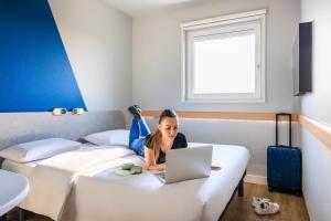 a woman laying on a bed with a laptop at Ibis budget Lausanne-Bussigny in Lausanne