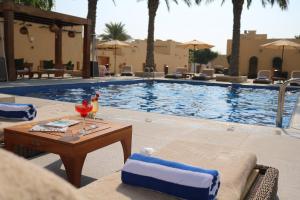 ドーハにあるSouq Al Wakra Hotel Qatar By Tivoliのテーブルサイドの隣にテーブルと椅子のあるスイミングプールを併設しています。